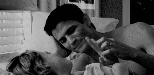 Man holds woman's hand while lying in bed gif